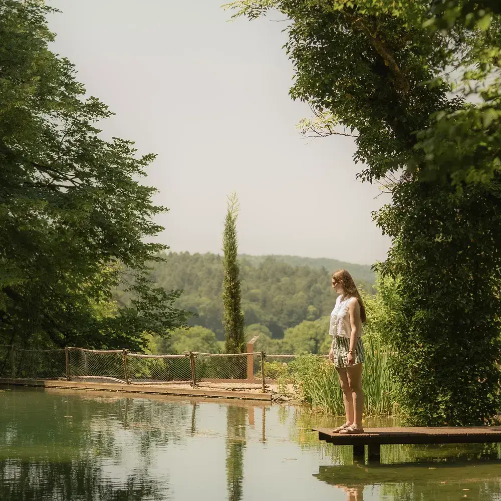 Pauline au bout d'un ponton, étang bordé de cyprès, lumière d'été.