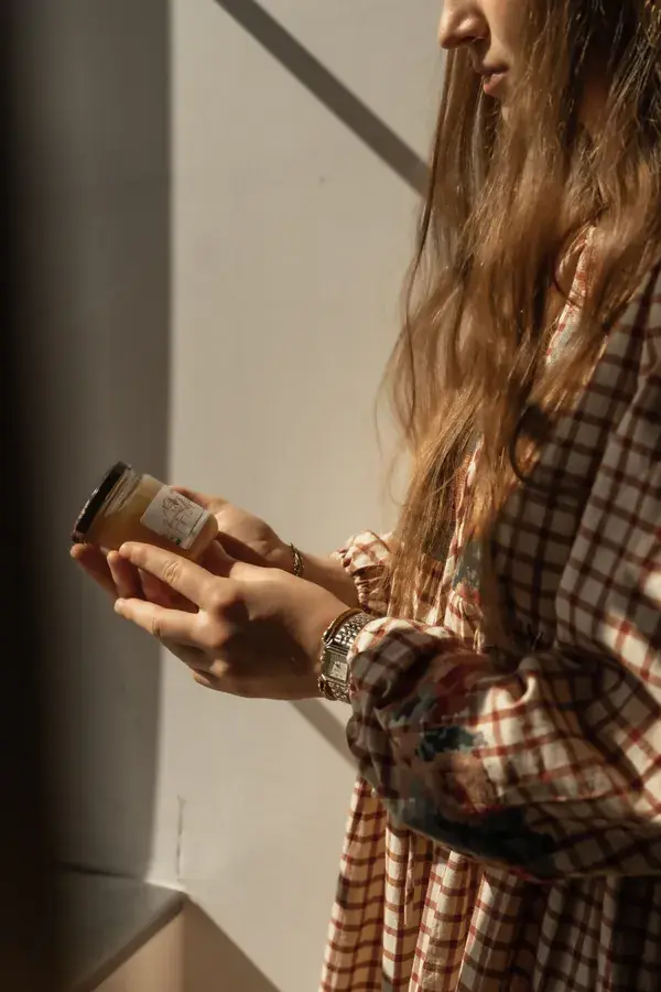 Pauline présente un pot de soin, produit en mains, lumière naturelle rasante.