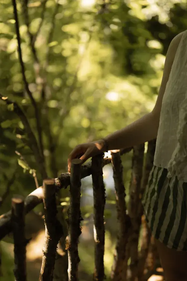 Sur un balcon en bois face à la forêt, main sur la rambarde, lumière d'été.